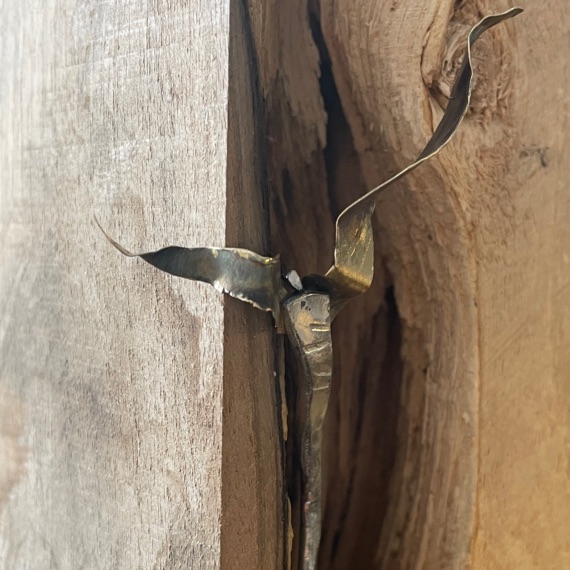 Filigrane Metallfigur mit ausgebreiteten Flügeln vor einer natürlichen Holzspalte