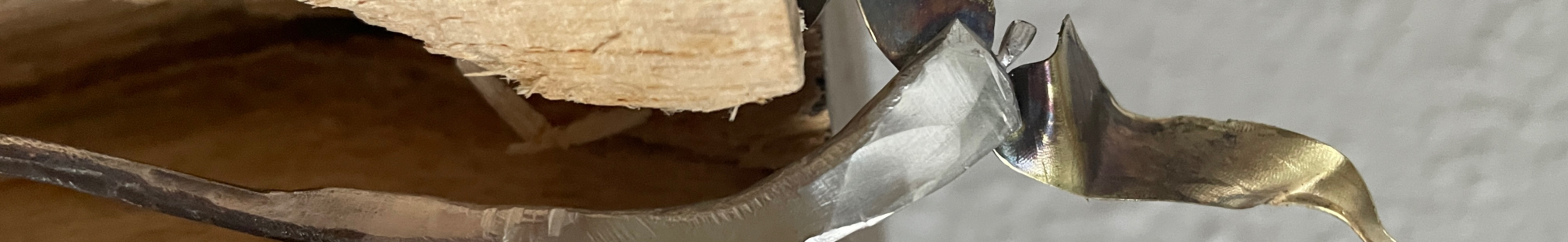 Nahaufnahme einer geschwungenen silberfarbenen Metallform neben einer hellen Holzfläche.