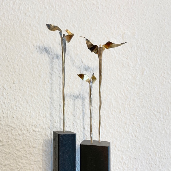 Mehrere filigrane, geflügelte Metallfiguren auf zwei unterschiedlich hohen dunklen Sockeln