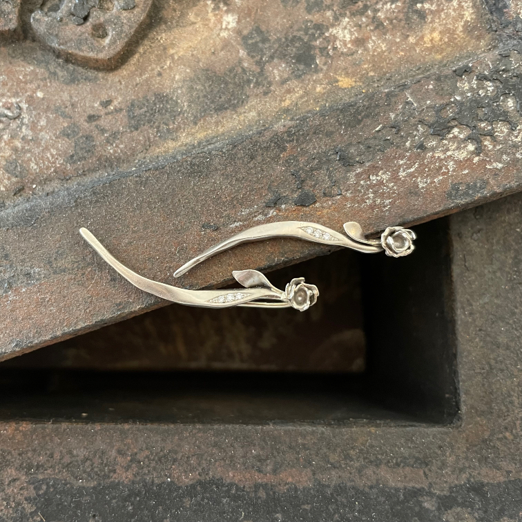 Zwei geschwungene, silberfarbene Schmuckstücke mit Blättern und kleinen Rosen auf dunklem Metall