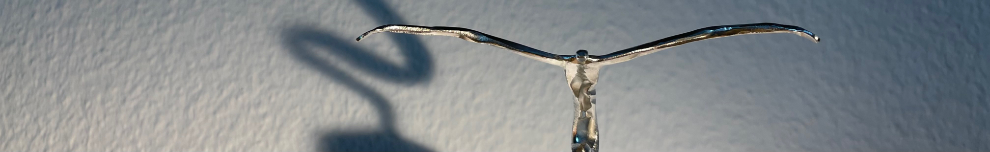 Nahansicht einer filigranen Metallfigur mit ausgebreiteten Armen und ihrem Schatten an der Wand.