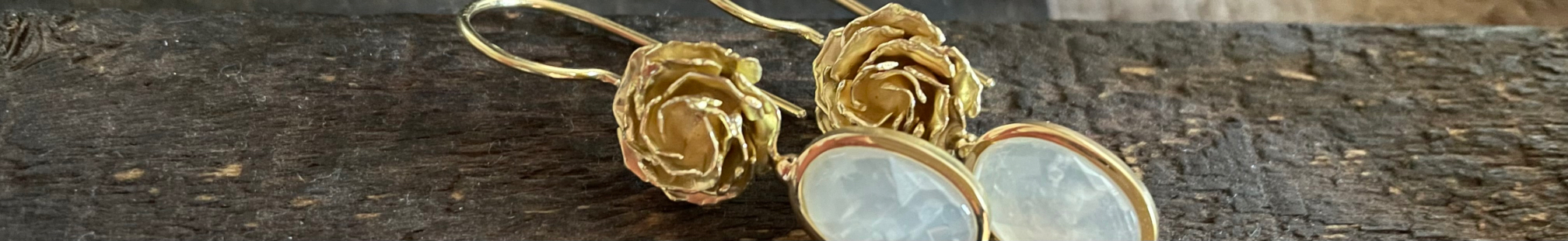 Detail von goldfarbenem Ohrschmuck mit plastischen Rosen und hellen Tropfenförmigen Anhängern