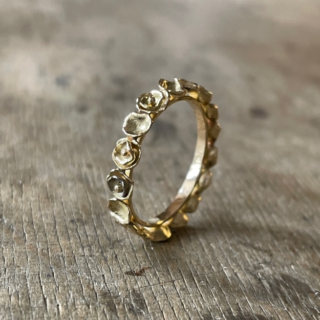 Goldfarbener Ring aus aneinandergereihten kleinen Blüten mit hellen Steinen auf einer Holzfläche.